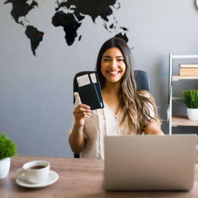 I am here to help you with your booking and travel questions. Female sales agent holding plane tickets while smiling and making eye contact at the travel agency