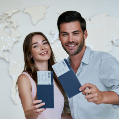 Portrait of joyful glad couple holding passport with flying tickets in hands pointing with forefinger looking at camera on map background