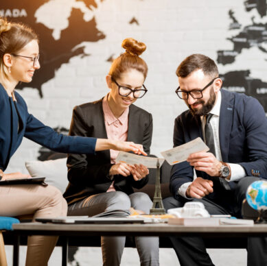 Young businesscouple choosing a trip with agent sitting at the travel agency office with world map on the background